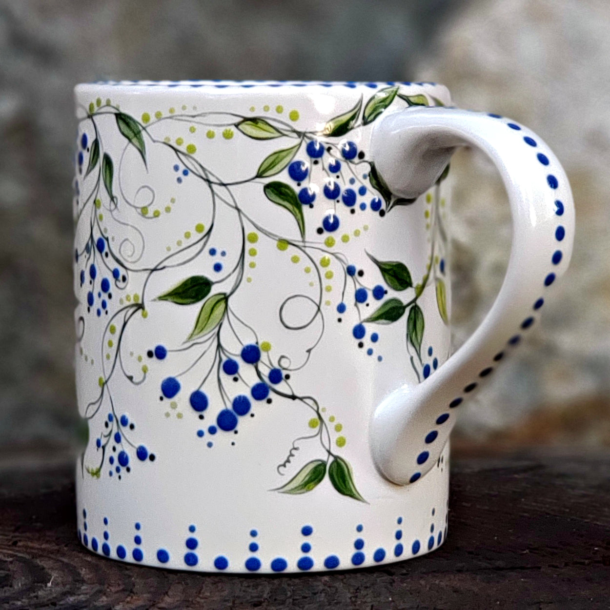 Hand painted 16 oz. ceramic mug.. white background sweet little blue berries with green leaves and vines. A satin glaze covers this beautiful piece.